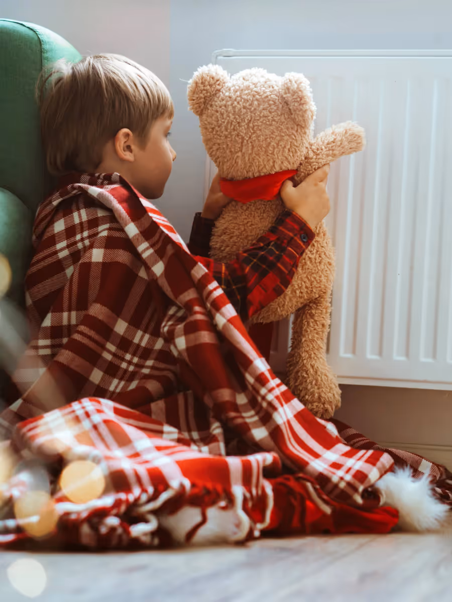 Kind mit Teddy sitzt vor einem Heizkörper – moderne Heiztechnik von Guhmann sorgt für Wärme und Sicherheit zu Hause.