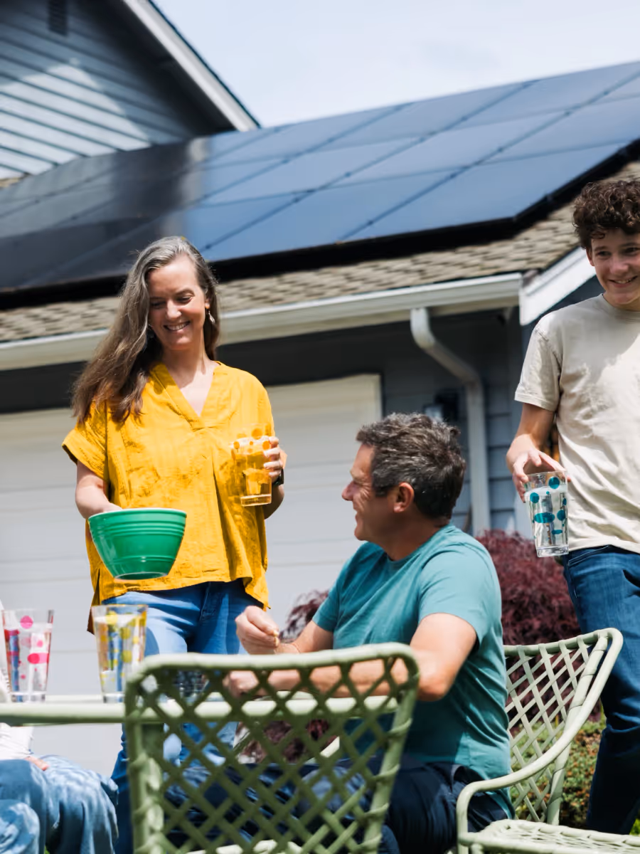 Familie sitzt im Garten vor einem Haus mit Solaranlage auf dem Dach.