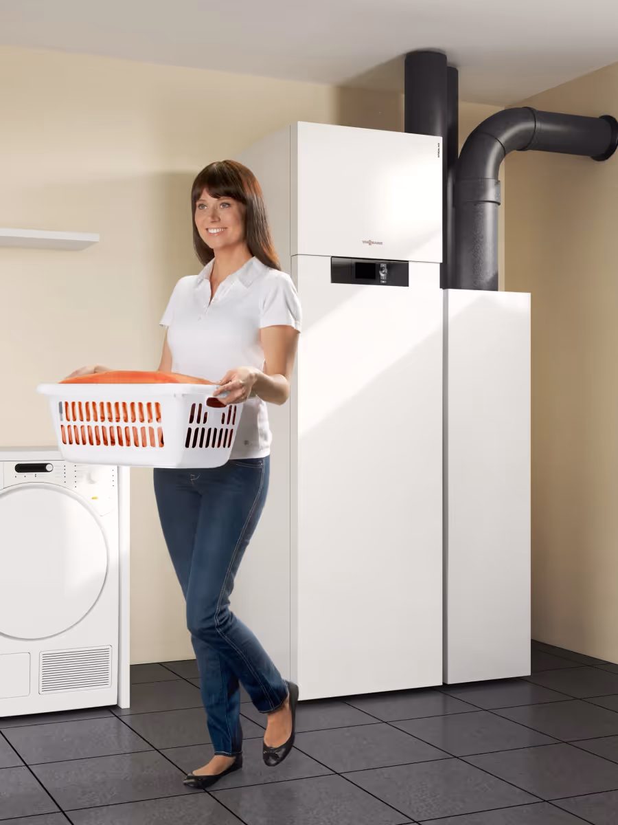 Lüftungsgerät in einem Hauswirtschaftsraum mit Waschmaschine und Wäschekorb.