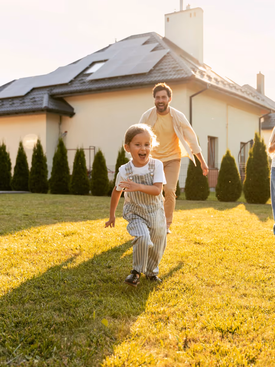 Vater spielt mit seinen Töchtern vor Haus mit Photovoltaikanlage auf dem Dach – Solarenergie und zukunftsfähige Haustechnik für die Familie von morgen.