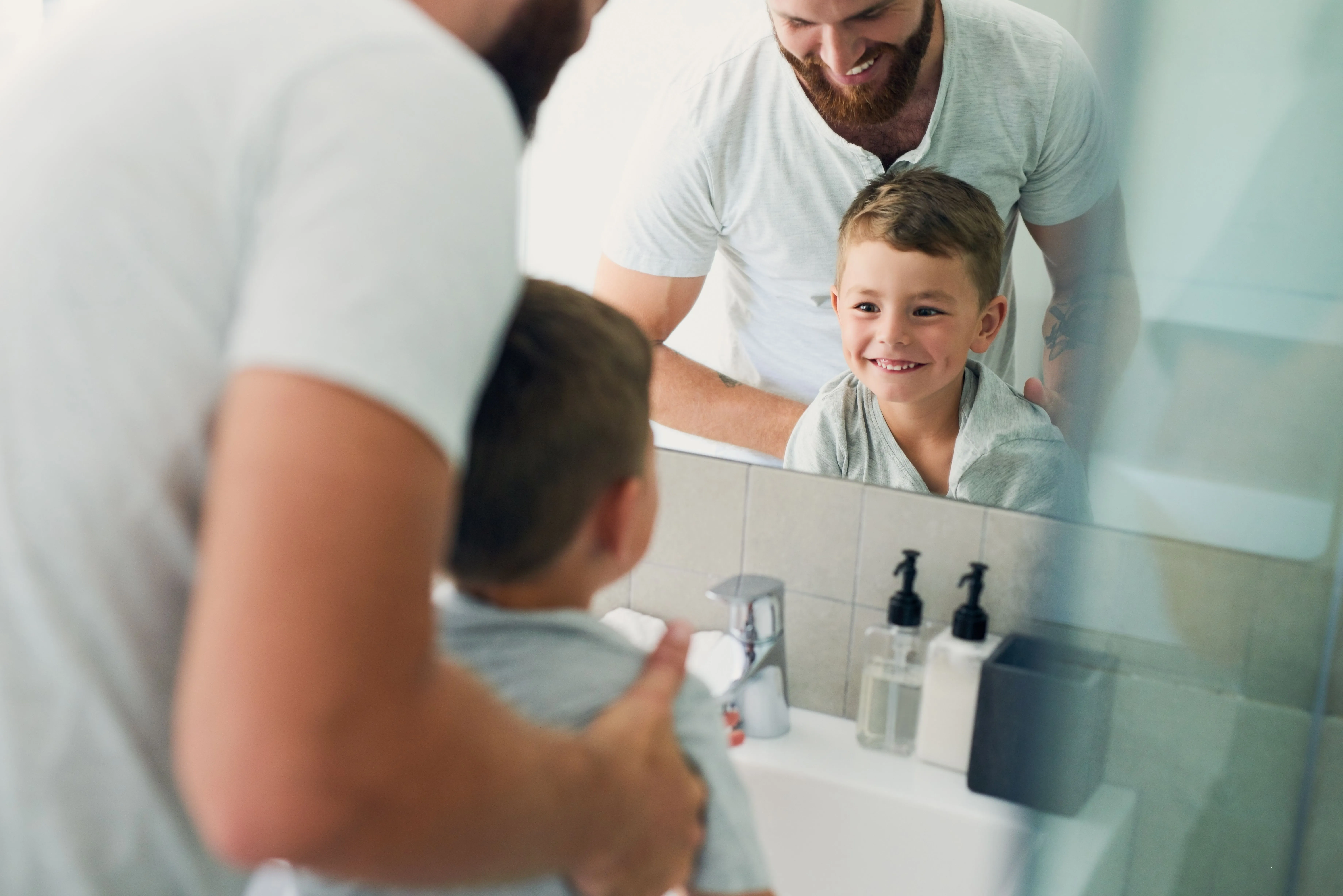 Vater und Sohn am Waschtisch vor dem Badezimmerspiegel mit verchromter Einhebelarmatur.