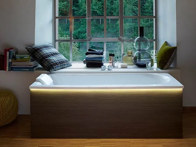 Beleuchtete Badewanne mit Holzverkleidung in einer gemütlichen Fensternische.