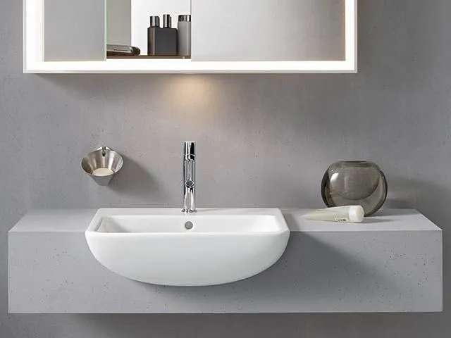 Halbrundes wandhängendes Waschbecken auf einer Betonkonsole unter einem beleuchteten Spiegelschrank.