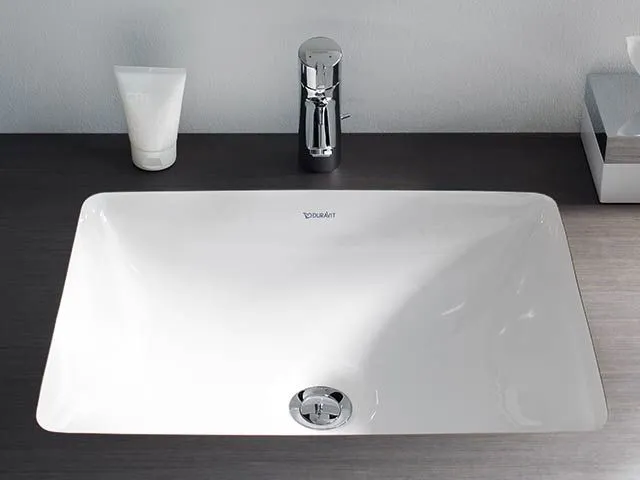Rechteckiges weißes Unterbau-Waschbecken mit hoher verchromter Armatur auf einer dunklen Holzplatte.