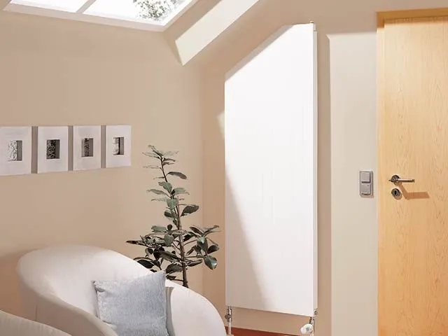Weißer abgeschrägter Heizkörper neben einer Holztür in einem hellen Wohnraum mit Dachfenster.