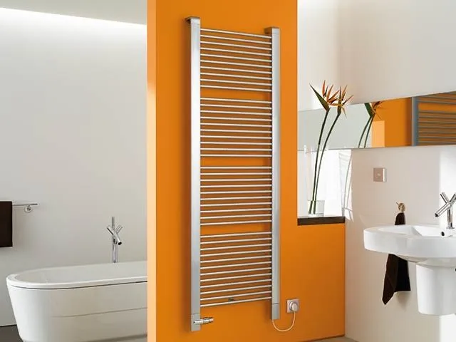 Verchromter Sprossen-Handtuchheizkörper an einer orangefarbenen Wand zwischen Badewanne und Waschtisch.