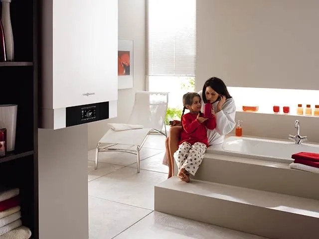Mutter und Kind an der Badewanne neben einem wandhängenden Gas-Brennwertgerät im hellen Bad.