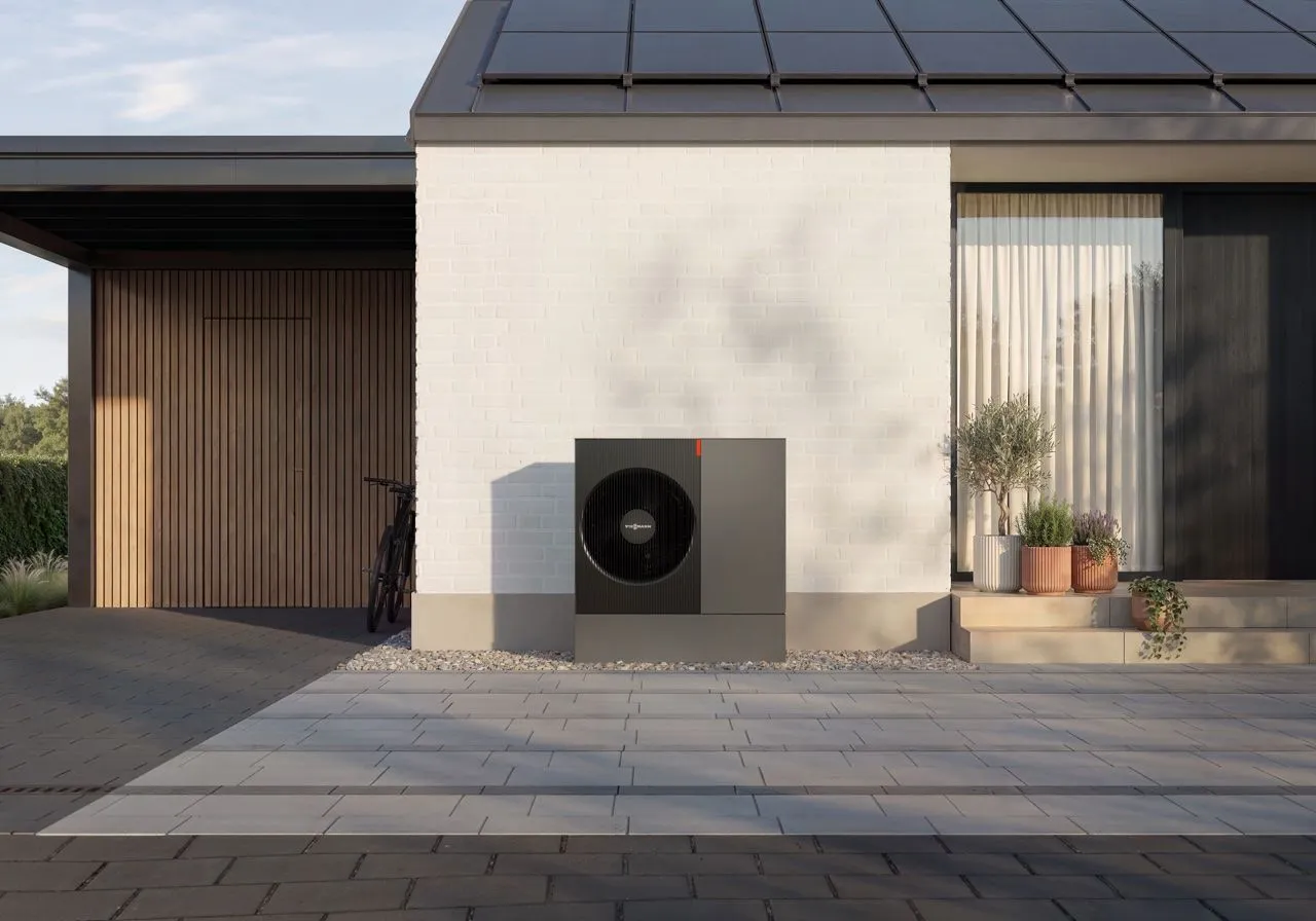Schwarze Monoblock-Wärmepumpe an der Fassade eines modernen Hauses mit Photovoltaikanlage auf dem Dach.