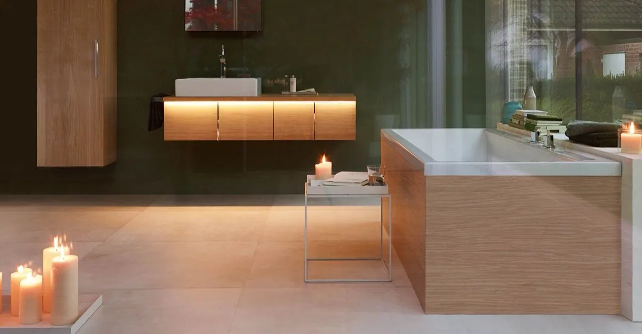 Stimmungsvolles Bad mit holzverkleideter Badewanne und beleuchtetem Eichen-Waschtisch bei Kerzenschein.