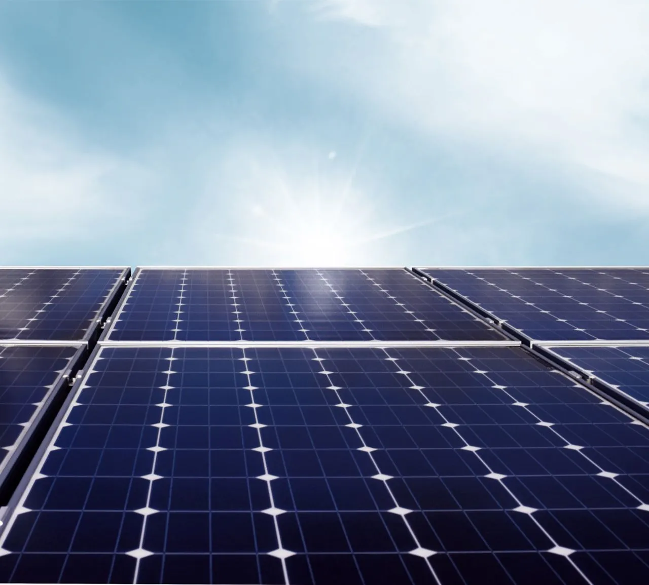Sonnenlicht über den blauen Modulen einer Photovoltaikanlage vor blauem Himmel.