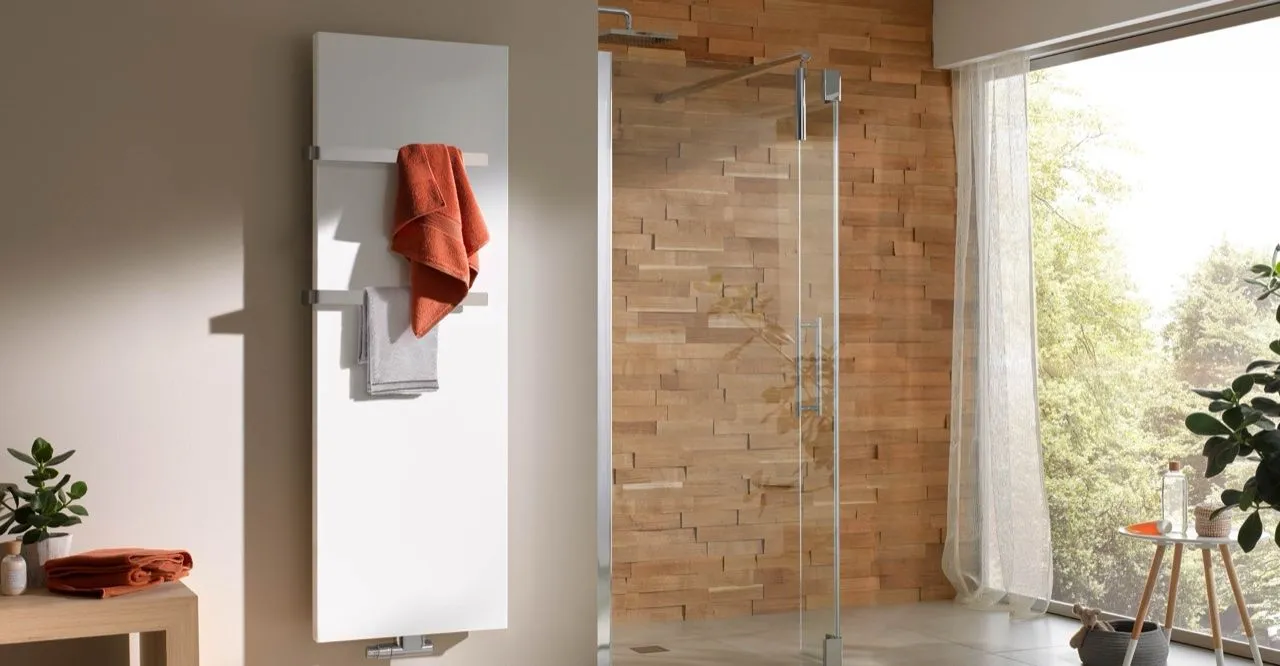 Weißer Design-Badheizkörper mit Handtüchern neben einer holzverkleideten Dusche.