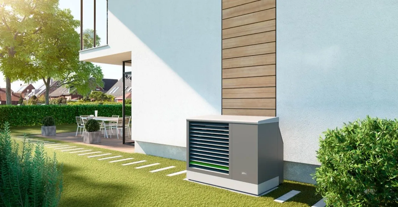 Außengerät einer Luft-Wärmepumpe neben einem modernen Wohnhaus mit Garten.