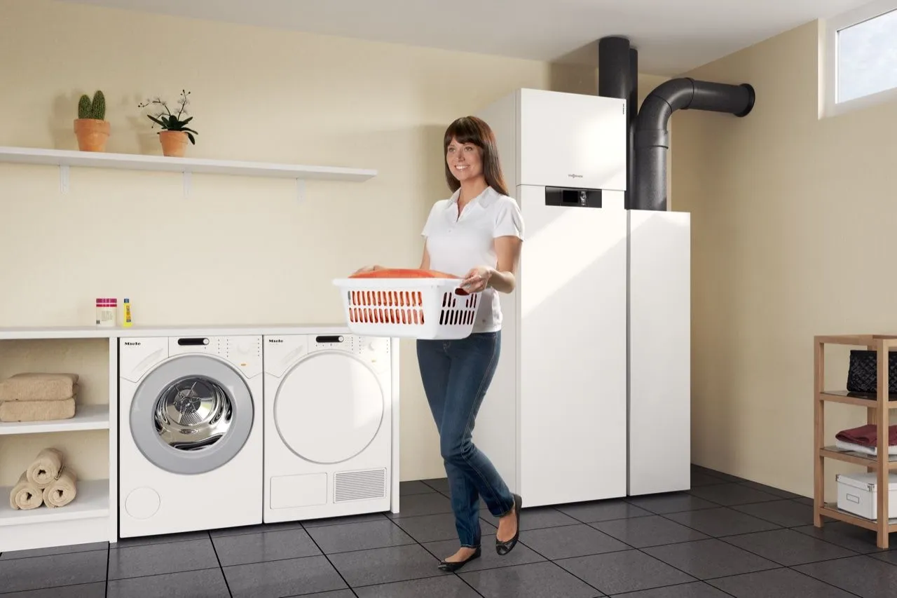 Frau mit Wäschekorb im Hauswirtschaftsraum neben einer Wärmepumpe mit Wohnraumlüftung.