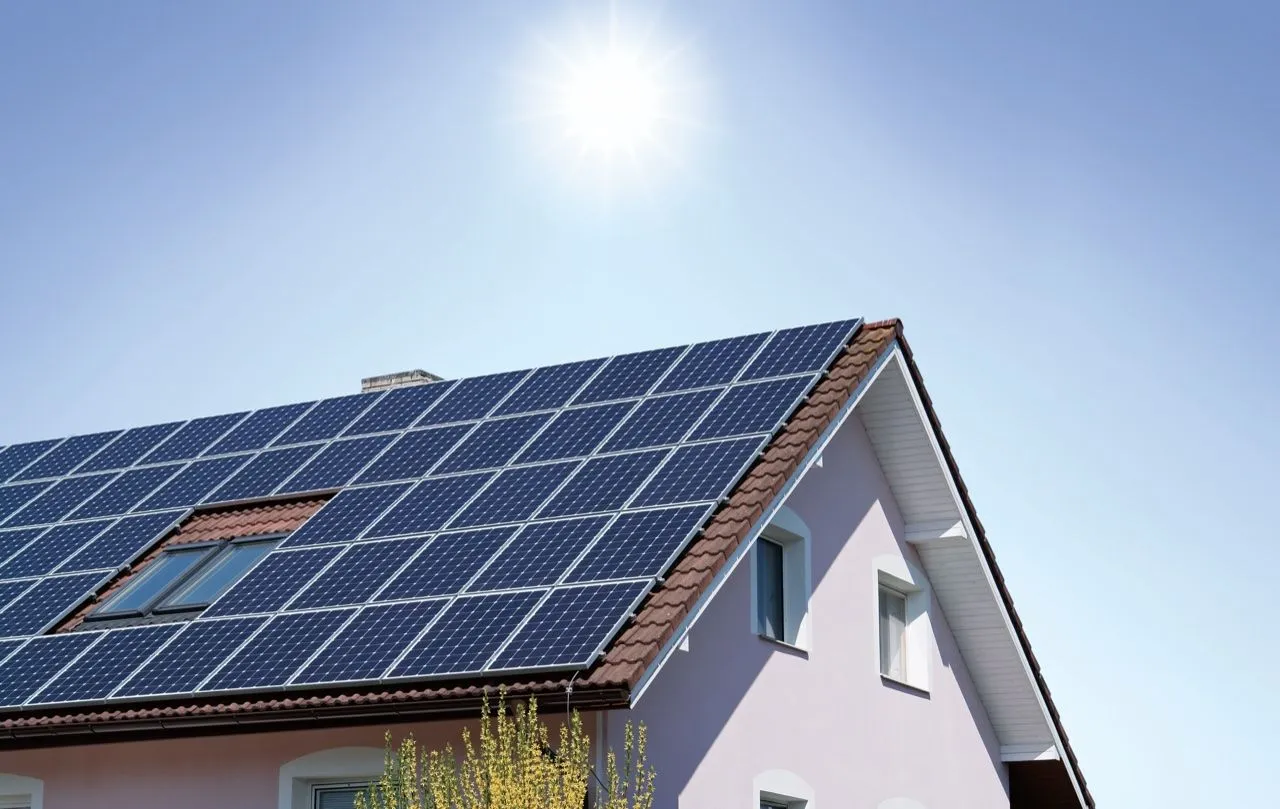 Sonne über dem vollflächig mit Photovoltaikmodulen belegten Satteldach eines Wohnhauses.