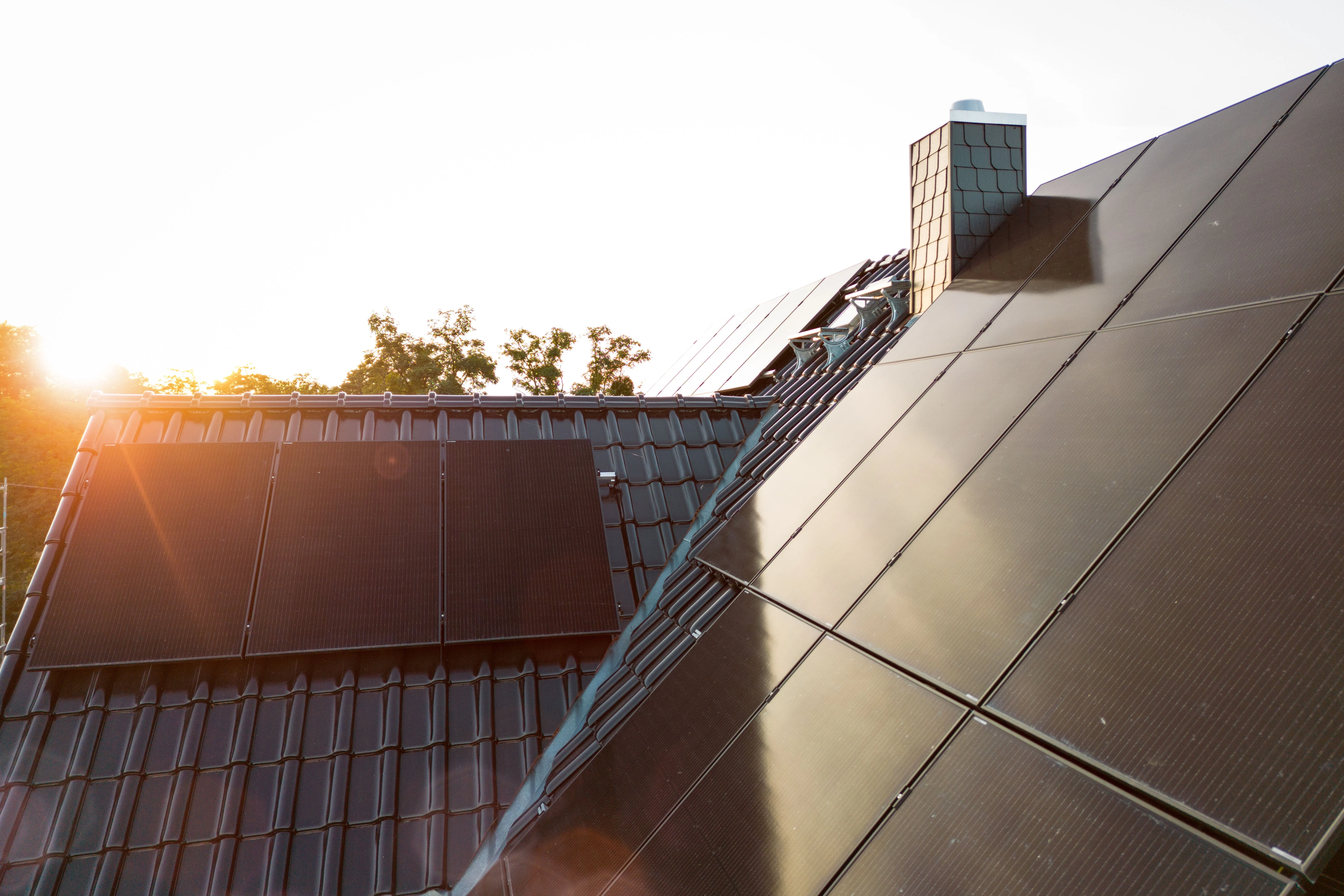 Dachfläche mit schwarzen Photovoltaikmodulen rund um einen Schornstein im warmen Abendlicht.