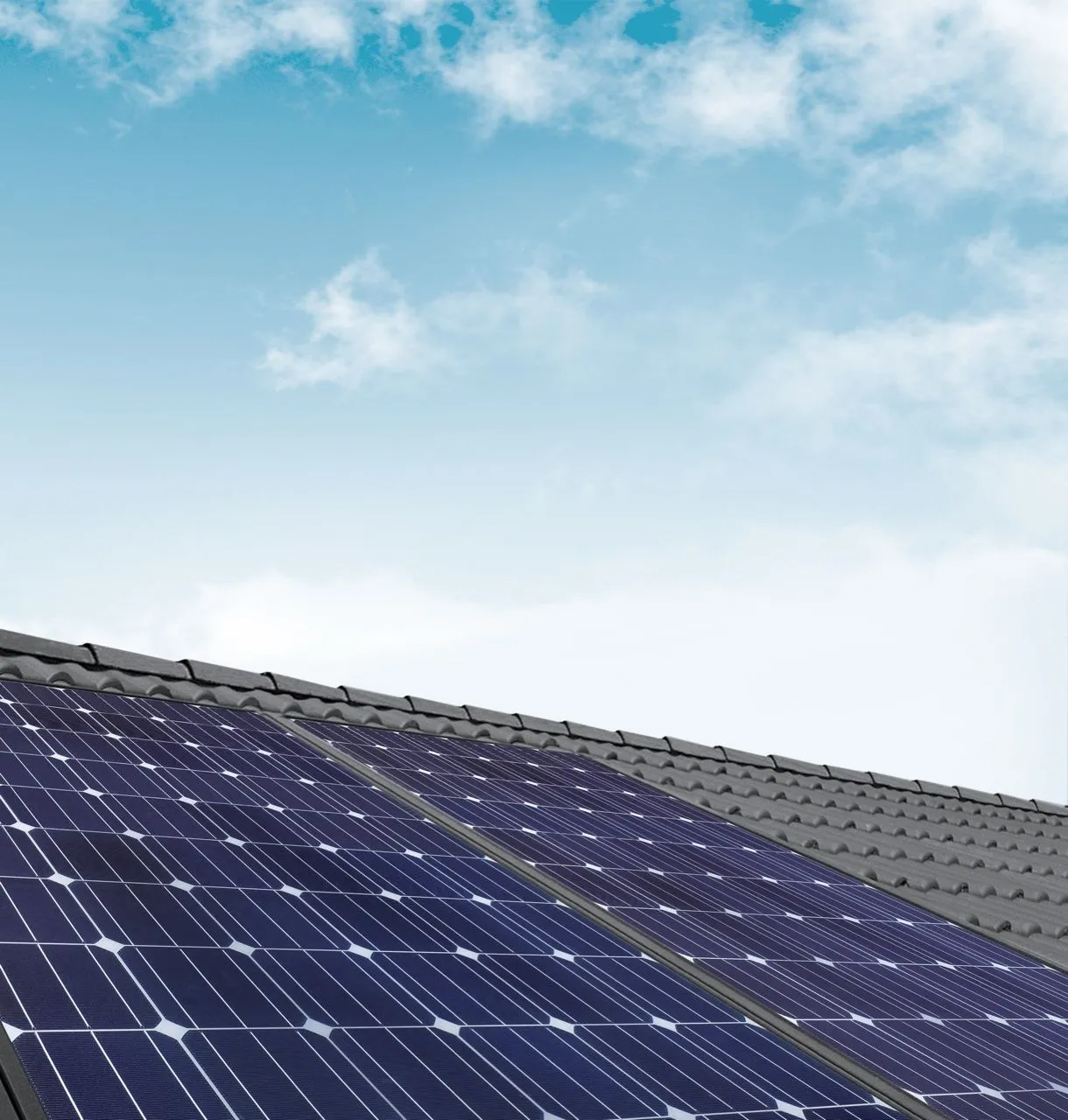 Photovoltaikmodule auf einem geneigten Ziegeldach vor blauem Himmel.
