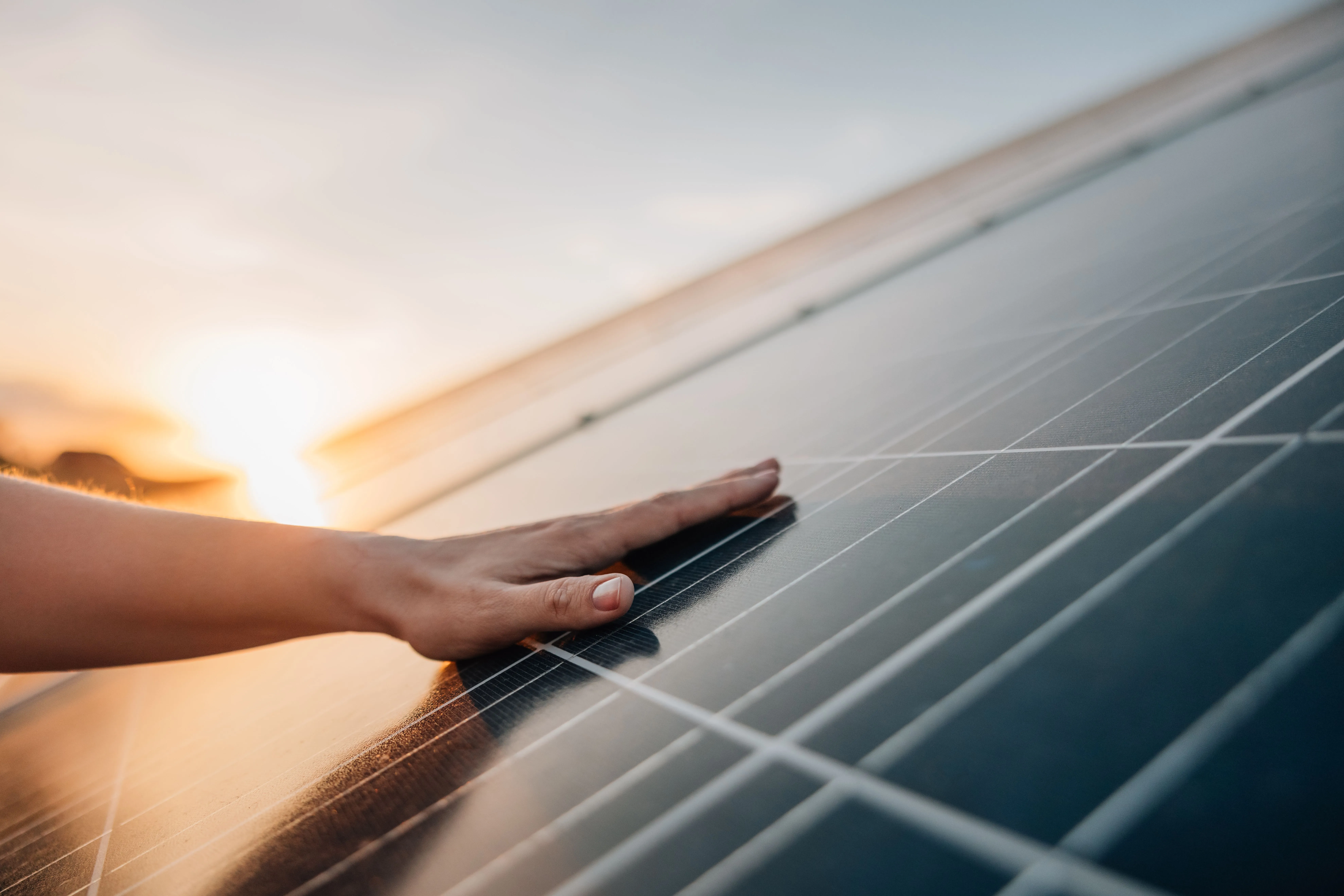 Hand berührt im Sonnenuntergang ein Photovoltaikmodul auf einem Dach.