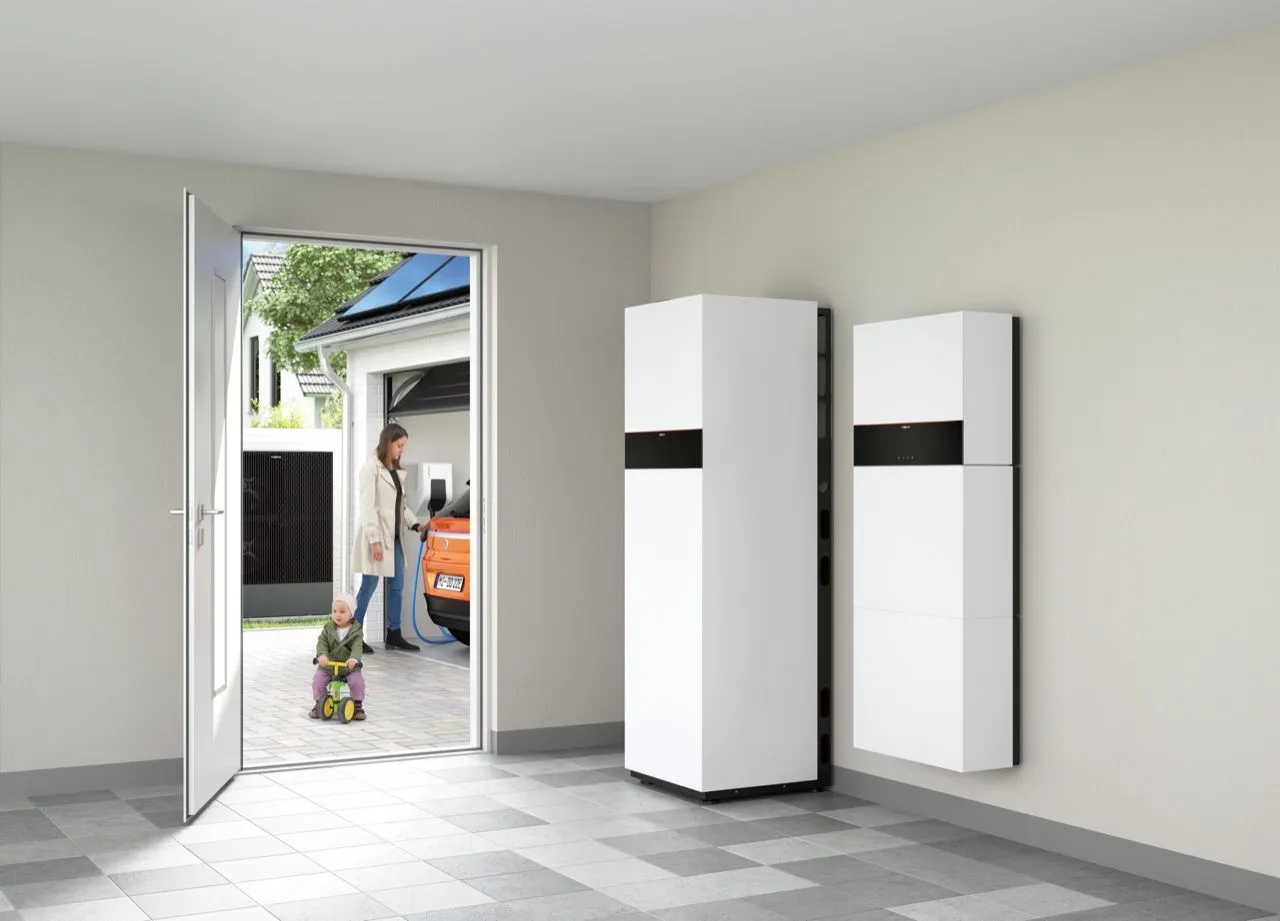 Heller Technikraum mit Stromspeicher und Energiezentrale; durch die offene Tür lädt eine Mutter mit Kind das Elektroauto.