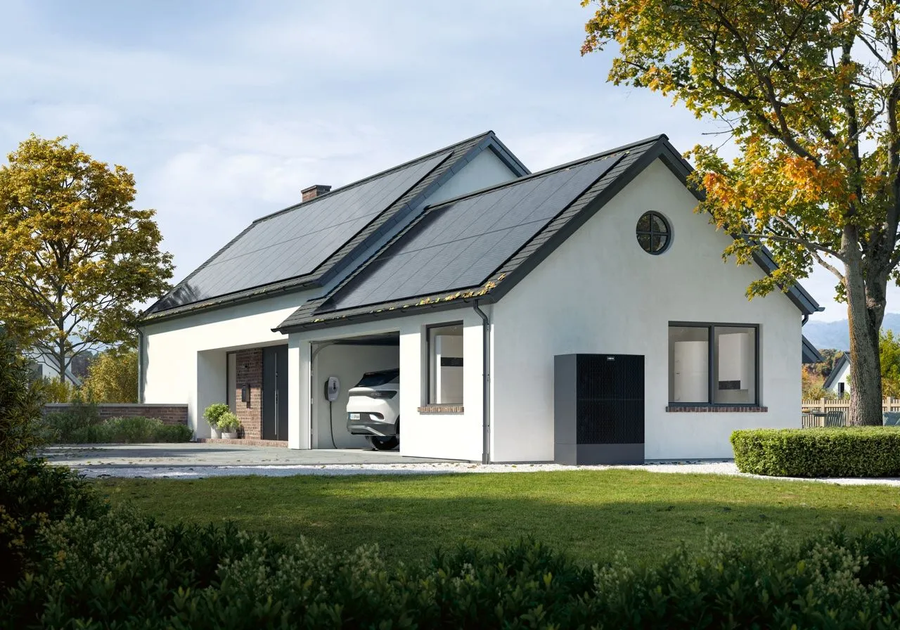 Weißes Einfamilienhaus mit Photovoltaikdach, Elektroauto an der Wandladestation in der Garage und Wärmepumpe an der Fassade.